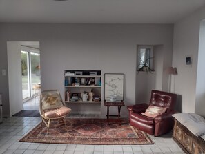 A living room with a bookshelf, a red leather chair, a patterned rug, and a wooden cabinet. - Character house with 180° panoramic sea view - Côte Sauvage de Portsall (Landunvez)