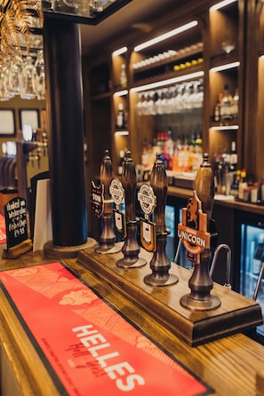 A bar area with multiple beer taps, a wooden counter, and a red sign with 'HELLES' on it.