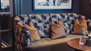 A sofa with a geometric patterned cover, a framed artwork above it, and a round wooden table beside it. - The Wheatley Arms (Ilkley)