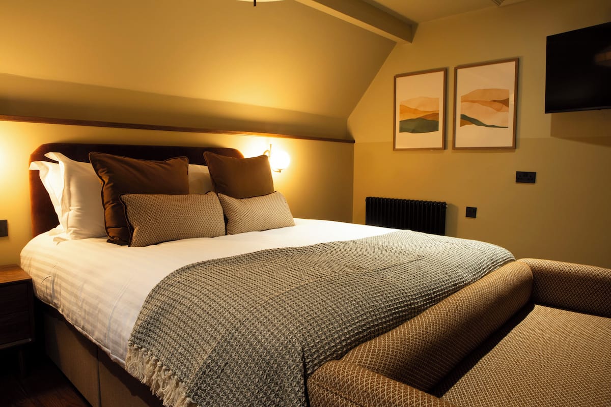 A bedroom with a bed, pillows, a blanket, a nightstand, and a wall-mounted TV.