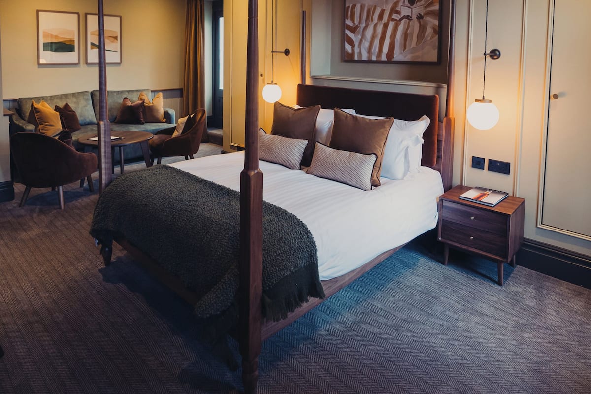 A hotel room with a large bed, a desk, a sofa, and a wall-mounted artwork.