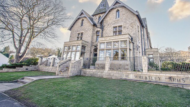 A large stone building with a prominent tower, a stone staircase leading to the entrance, and a well-maintained lawn. - The Wheatley Arms (Ilkley)