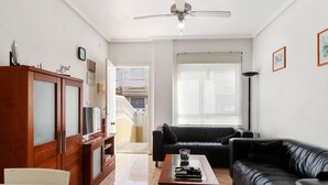 Een woonkamer met een zwarte leren bank, een houten salontafel, een televisie op een houten kast en een plafondventilator.