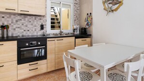 Een moderne keuken met houten kastjes, een zwarte oven, een witte eettafel met stoelen en een decoratief wandobject.