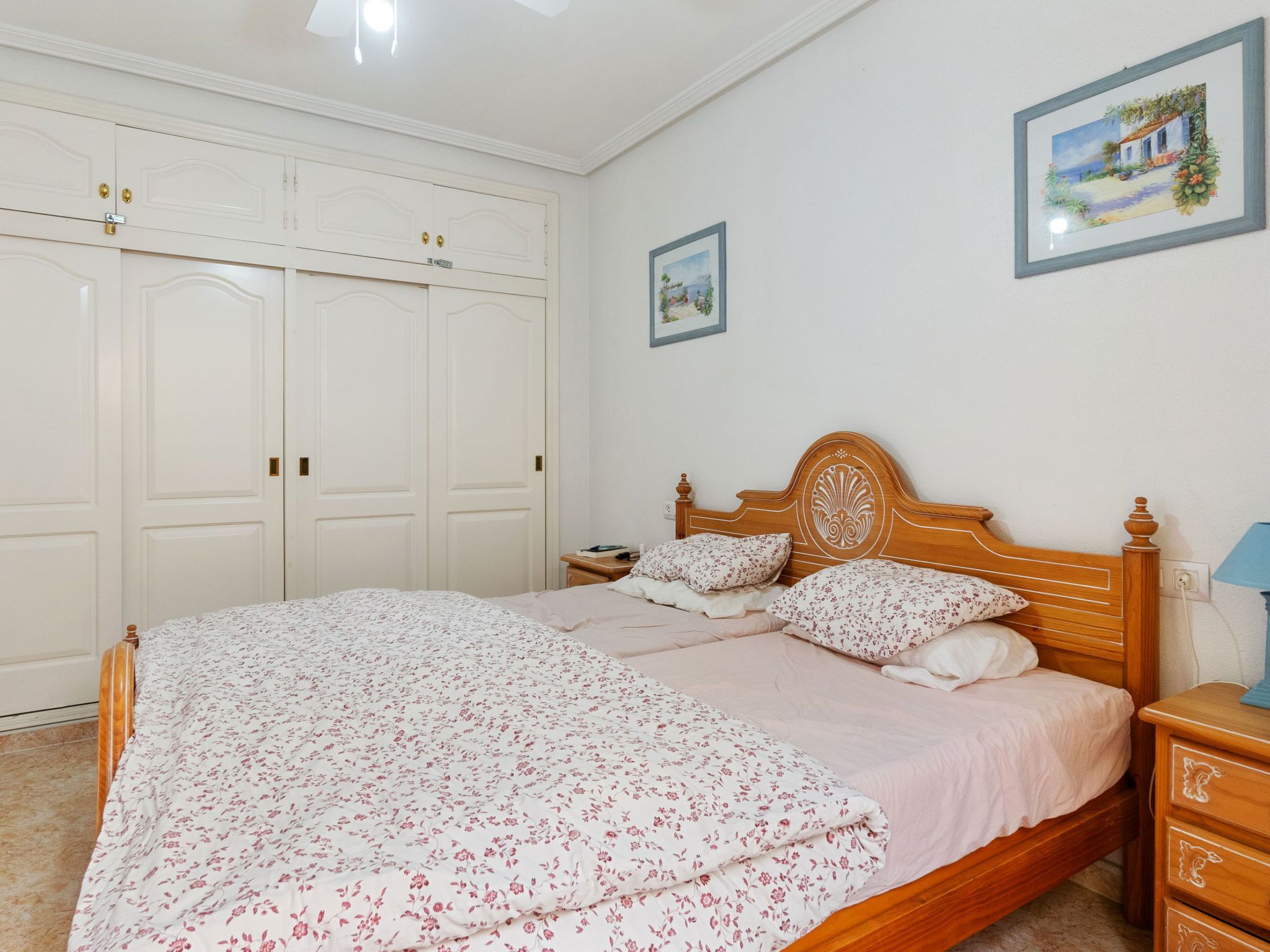 A bedroom with a wooden bed, a nightstand, a wardrobe, and two framed pictures on the wall.