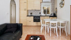 Een compacte keuken met houten kastjes, een inbouwoven en een eethoek met witte stoelen en een tafel.