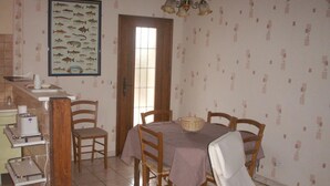 A dining area with a wooden table, chairs, a chandelier, and a fish-themed wall hanging. - Charming cottage near the Sioule River with private garden (Saint-Germain-de-Salles)