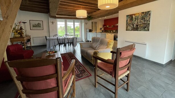 Una sala de estar acogedora con comedor, vigas de madera, un sofá rojo y un cuadro en la pared.