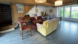 Un salón espacioso con techos altos, vigas de madera, chimenea, sofá, mesa de centro y comedor con vistas al exterior.