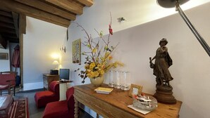 Una habitación con una mesa de madera, sillas rojas, una estatua, un jarrón con flores, una lámpara y un cuadro en la pared.