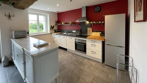 Una cocina con armarios blancos, un refrigerador de acero inoxidable, un horno empotrado y una ventana con vistas a la vegetación.