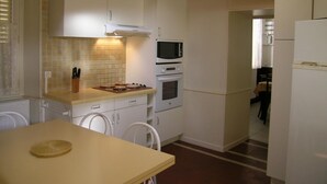 Une cuisine de taille réduite avec des meubles blancs, un four à micro-ondes, un four traditionnel et une table avec des chaises.