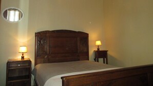 Une chambre avec un lit en bois, deux tables de chevet avec des lampes, un miroir rond et une bordure à motifs floraux au plafond.