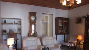 Un salon avec deux fauteuils blancs, une table basse en bois, une bibliothèque, une horloge et un meuble.