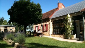 A rustic stone building with a metal roof, outdoor seating, and a large tree in the foreground. - Charming Renovated Farmhouse - Pets Welcome - Near Commentry (Beaune-d'Allier)