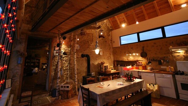 A rustic kitchen with exposed stone walls, wooden beams, and a large dining table. - Charming Renovated Farmhouse - Pets Welcome - Near Commentry (Beaune-d'Allier)