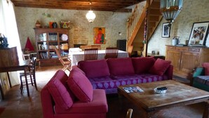 A cozy living room with a red sofa, wooden coffee table, and a staircase leading to an upper level. - Charming Renovated Farmhouse - Pets Welcome - Near Commentry (Beaune-d'Allier)