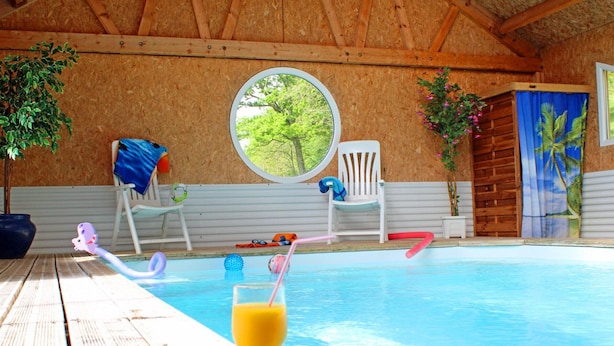 A wooden deck with a pool, a round window, and a chair with a towel. - Cozy house with pool and sauna in nature (Vernusse)