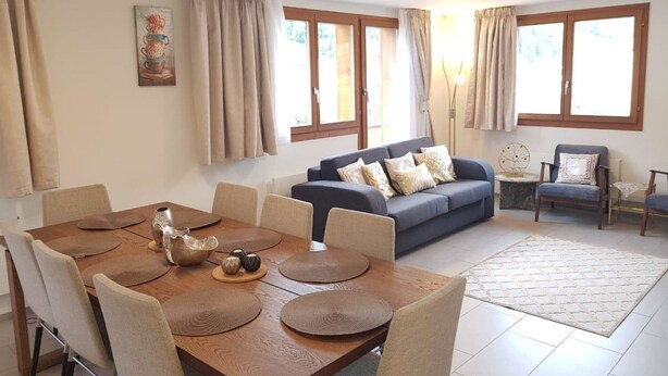 A modern living room with a dining area, large windows, and a sofa with decorative pillows.