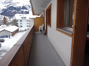 A balcony with a view of a snowy mountain, a parked car, and a building with a wooden facade.