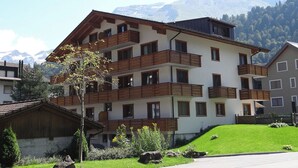 A multi-story building with balconies, a sloped roof, and a mountainous backdrop.