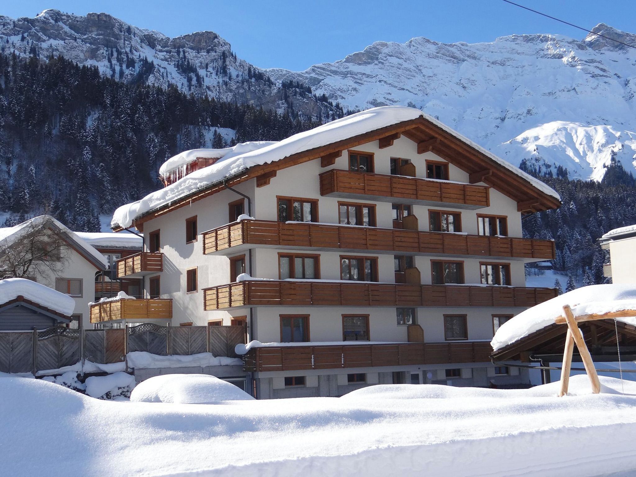 A multi-story hotel with balconies, set against a snowy mountain backdrop.