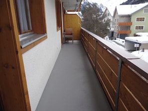 Een smal balkon met houten hekwerk, een stoel en uitzicht op omliggende gebouwen.