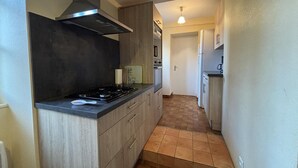 A narrow kitchen with a gas stove, wooden cabinets, and a black range hood. - Spacious lodging in La Guillermie, pets allowed, garden (La Guillermie)