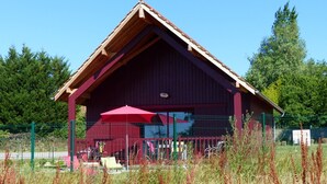 Un bâtiment rouge avec un toit en pente et une zone abritée sous un parasol rouge.