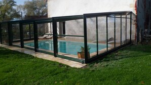 Une piscine dotée d’une enceinte en verre, entourée d’une pelouse et d’un bâtiment dont le toit est en pente.