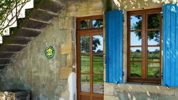 Un bâtiment rustique en pierre, doté d’une porte en bois, de volets bleus et d’un banc en pierre à l’extérieur.