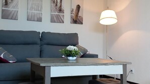 Un salon moderne avec un canapé gris, une petite table sur laquelle est posée une plante, et un lampadaire.