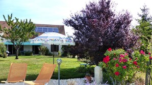 Un espace patio comprenant deux chaises longues, un parasol décoratif et un jardin avec des roses rouges et des fleurs violettes.