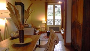 Una sala acogedora con una mesa de comedor de madera, sillas de mimbre, un sofá y un amplio ventanal con vistas a zonas verdes.
