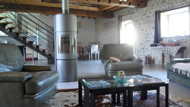 A cozy living room with a stone wall, a fireplace, a leather sofa, a glass coffee table, and a staircase. - Spacious lodge in historical hunting lodge with private garden (Chirat-l'Église)