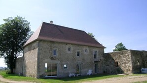 A stone building with a tiled roof, a glass door entrance, and a small outdoor seating area with chairs. - Spacious lodge in historical hunting lodge with private garden (Chirat-l'Église)