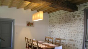 A dining area with a wooden table and chairs, a hanging light fixture, and a stone wall. - Spacious lodge in historical hunting lodge with private garden (Chirat-l'Église)