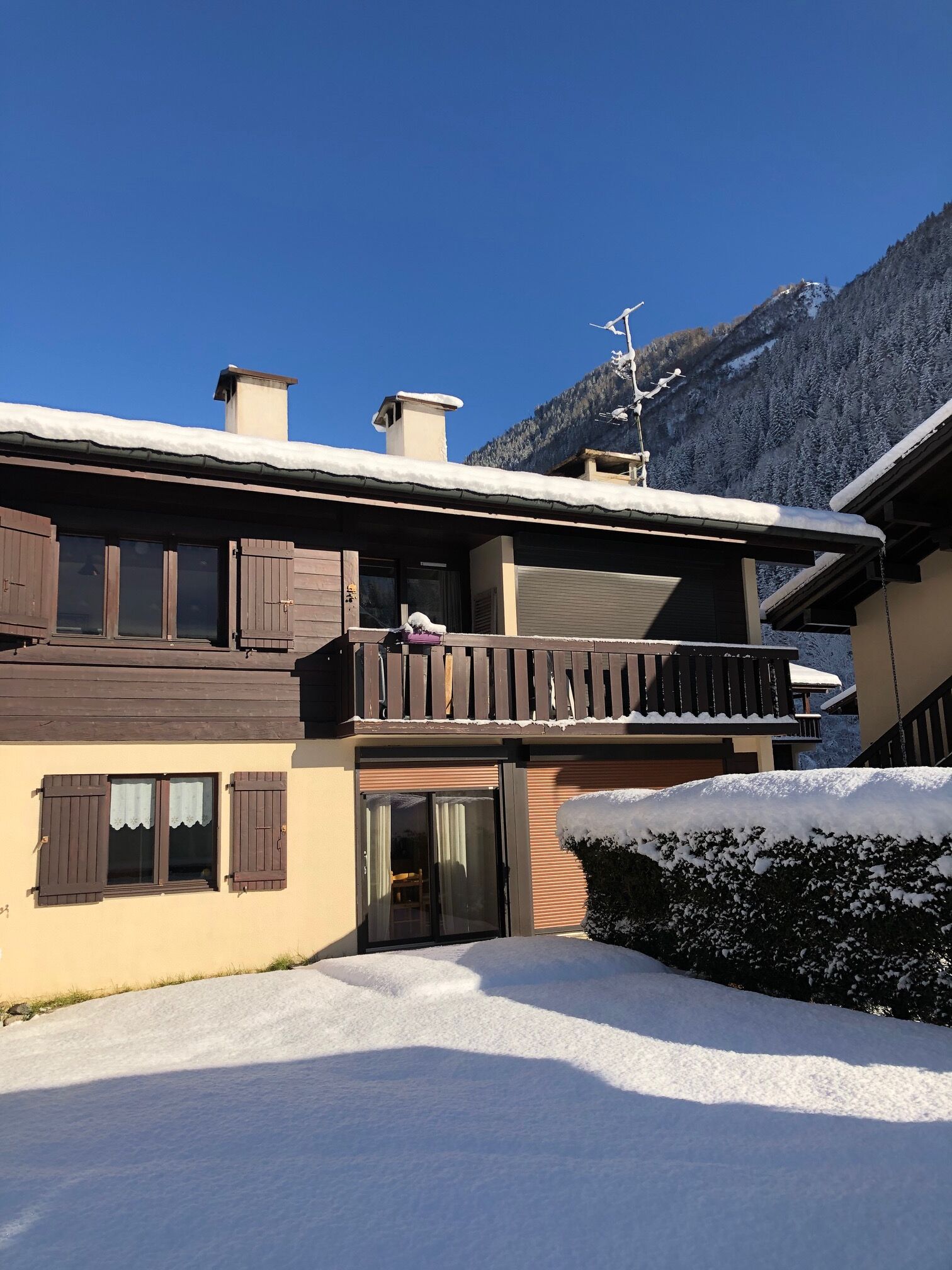 A two-story building with a balcony, wooden shutters, and a snow-covered roof.