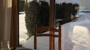 A wooden table with a plate and a glass bottle, a wooden chair, and a view of snow-covered mountains through a window. - Nice 2 rooms for 2 to 4 people in quiet hamlet with superb view on Mont-Blanc (Chamonix-Mont-Blanc)