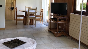 A cozy room with a wooden dining table, chairs, a TV on a wooden stand, a white floor lamp, and a wicker table with a decorative plate. - Nice 2 rooms for 2 to 4 people in quiet hamlet with superb view on Mont-Blanc (Chamonix-Mont-Blanc)