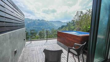 Relax on the balcony with a view of the surrounding mountains, featuring a hot tub and two comfortable chairs.