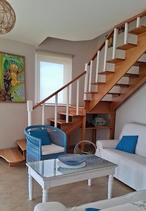 A living room with a staircase, a white sofa, a blue chair, and a glass coffee table. - Villa Bella Vista—Panoramic Sea View near Tropea (Zambrone)