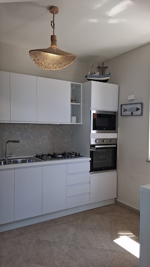 A modern kitchen with white cabinets, a gas stove, an oven, a microwave, and a hanging light fixture. - Villa Bella Vista—Panoramic Sea View near Tropea (Zambrone)