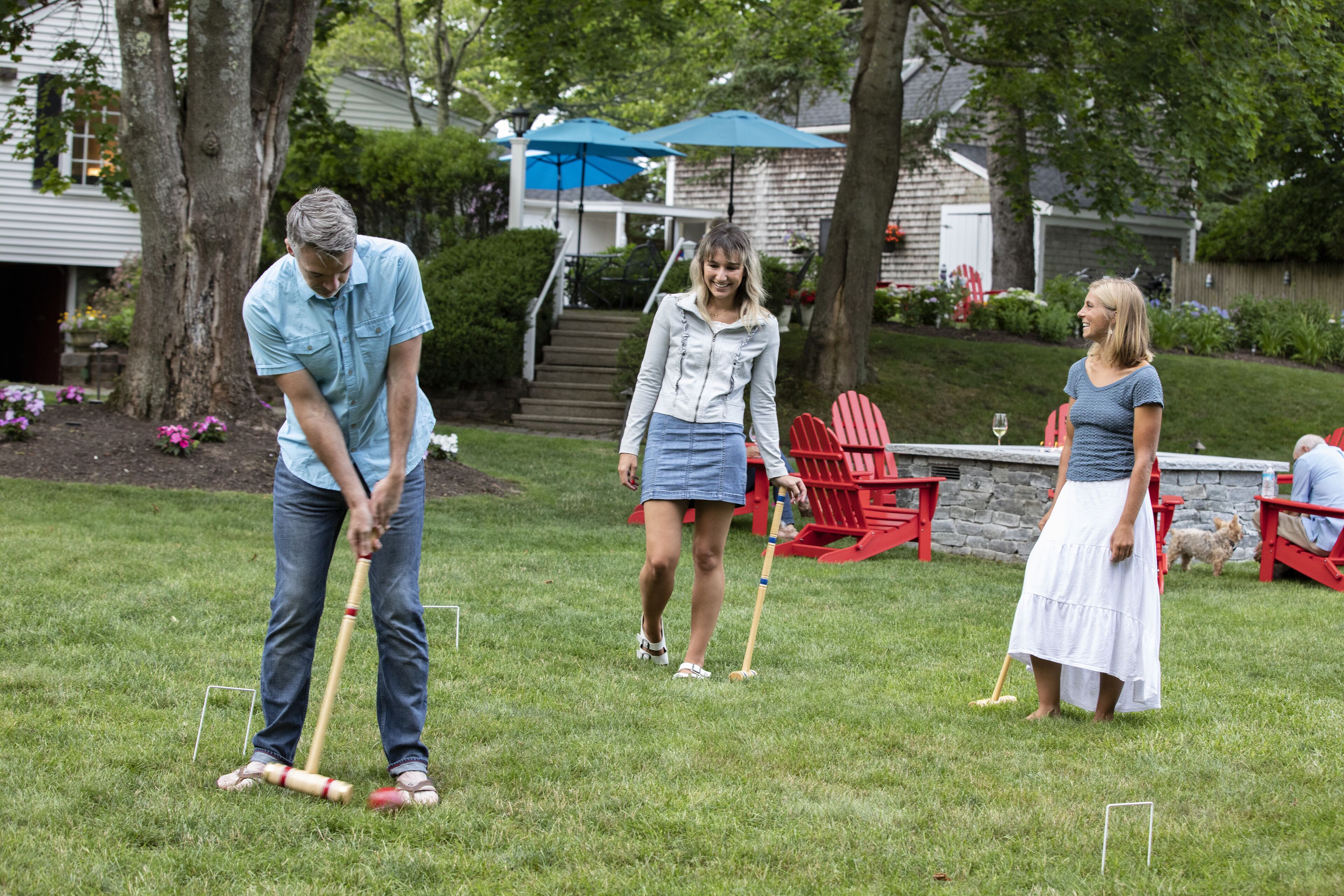 A grassy outdoor area with a croquet set up, a red Adirondack chair, and a stone wall in the background.