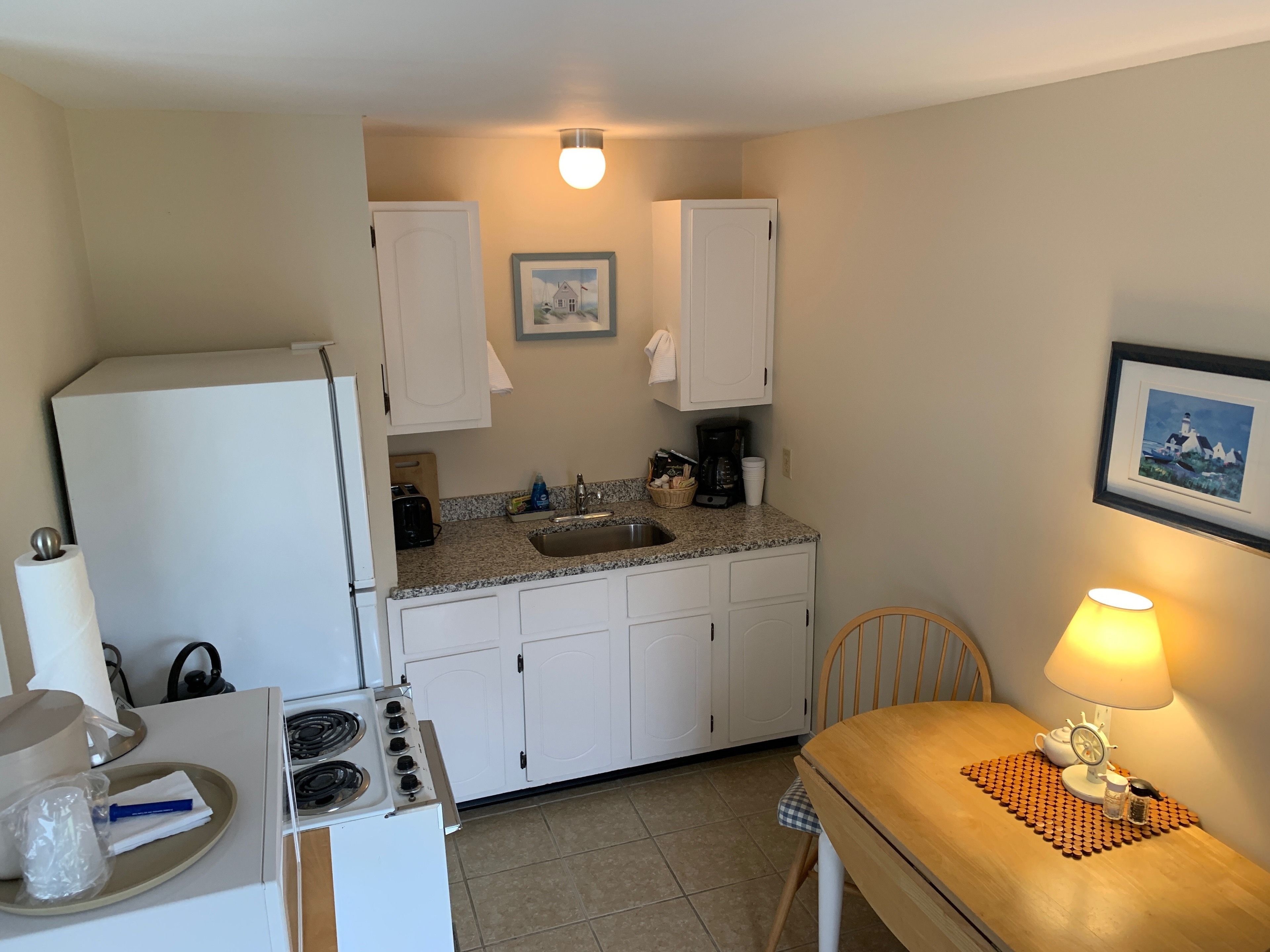 A compact kitchen with white cabinets, a stove, a sink, and a dining area with a table and chair.