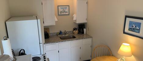 A compact kitchen with white cabinets, a stove, a sink, and a dining area with a table and chair.