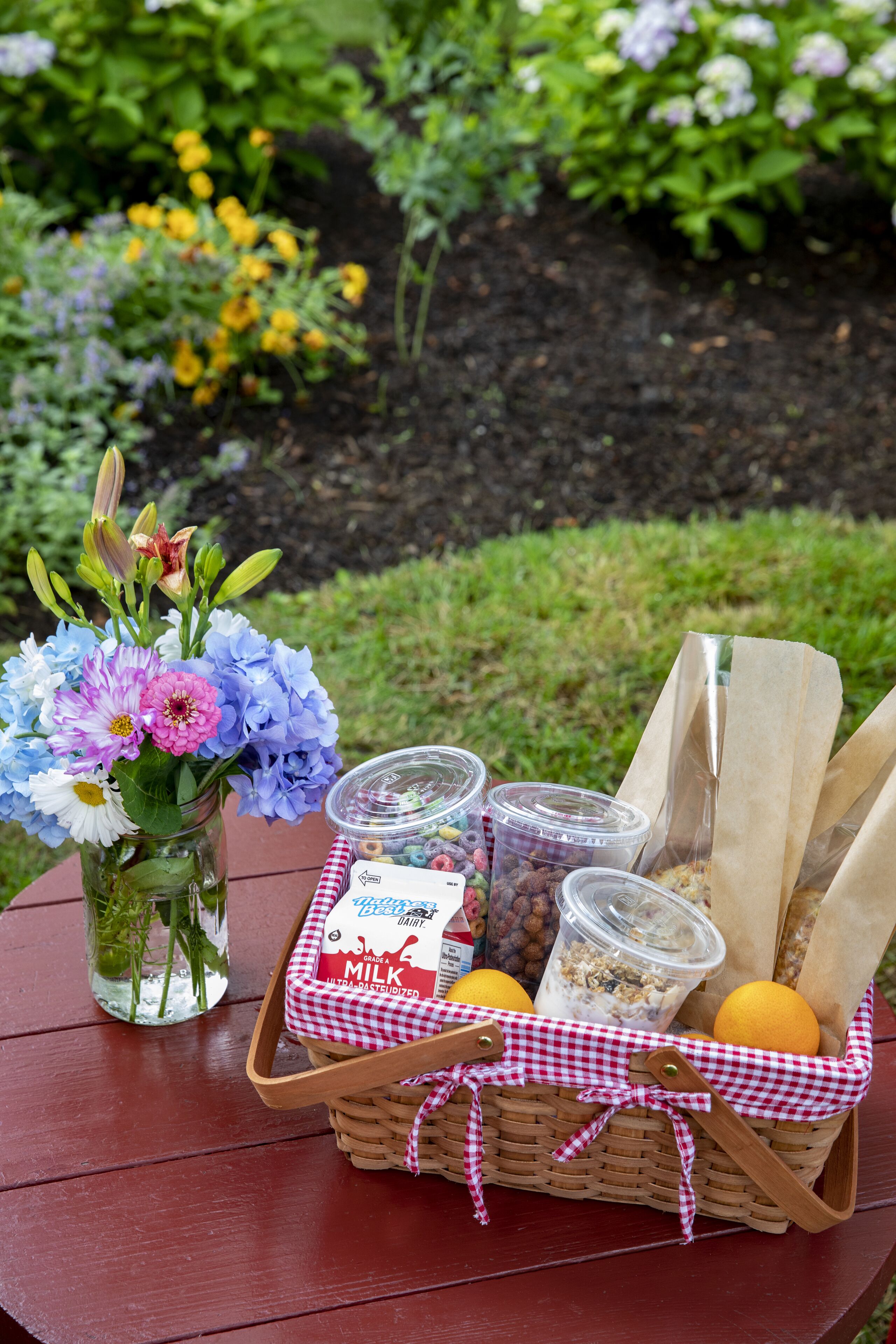 Ein Picknick mit Korb, der Milch, Beeren und Brot, einem Blumenvasen und einer Milchflasche enthält.