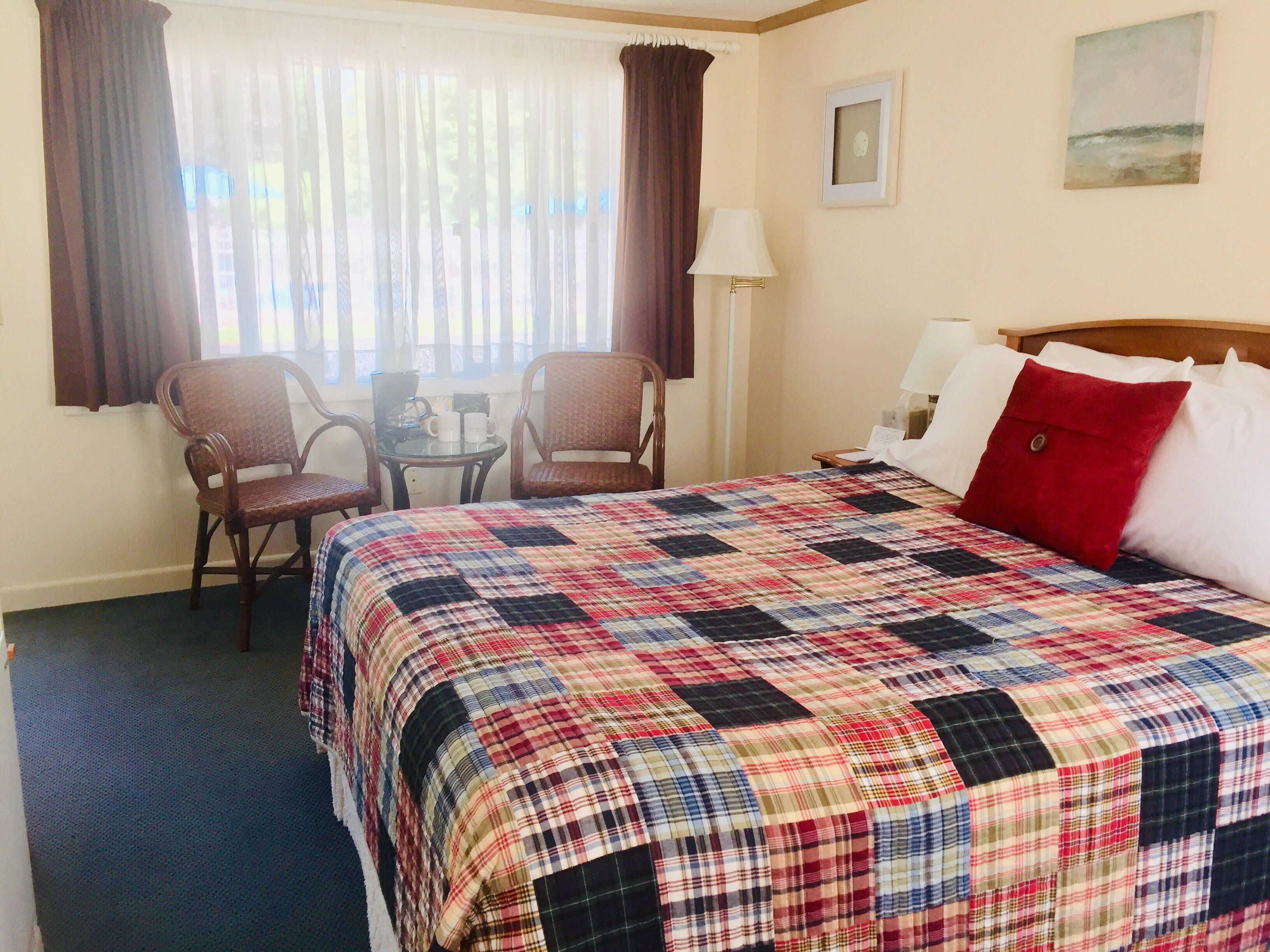 A hotel room with a large bed, a small table with chairs, a lamp, and a painting on the wall.