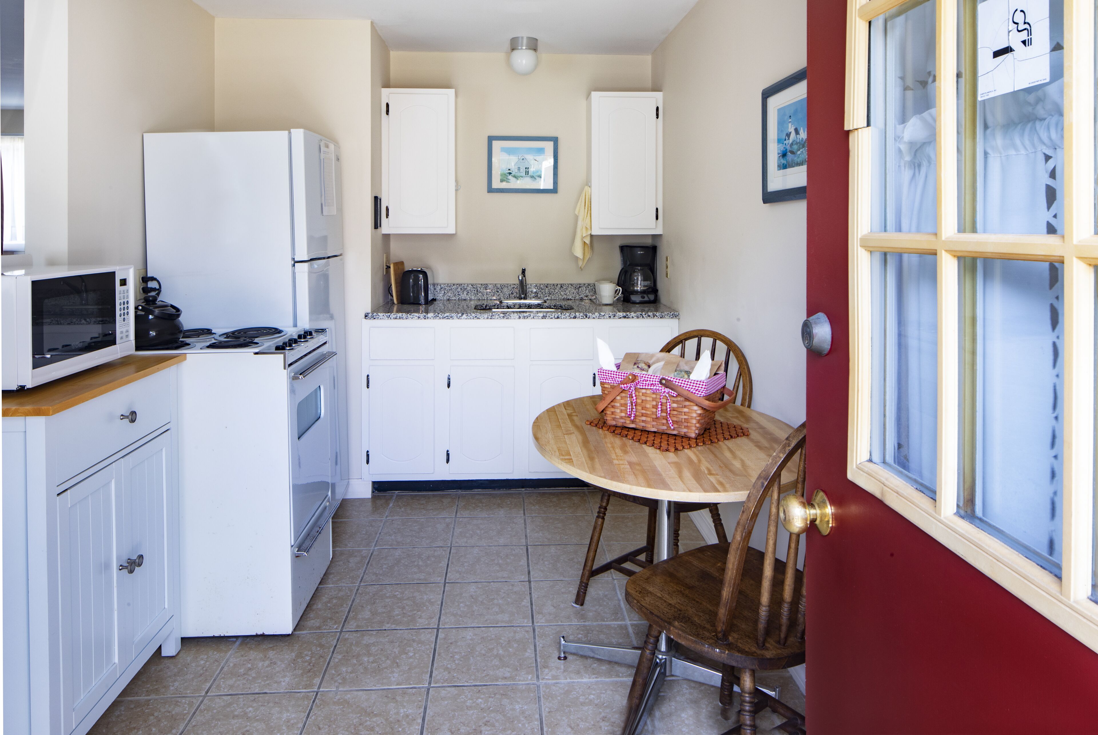 A compact kitchen with white cabinets, a microwave, a stove, and a sink. There is a dining table with chairs and a basket.