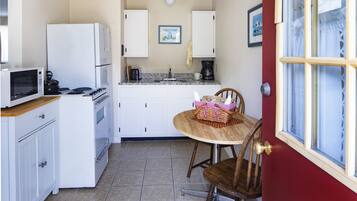 A compact kitchen with white cabinets, a microwave, a stove, and a sink. There is a dining table with chairs and a basket.
